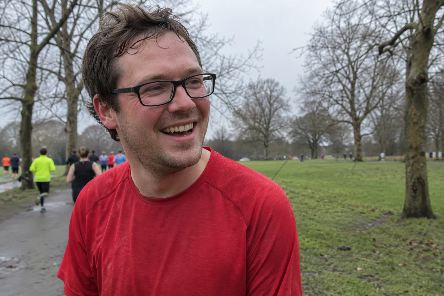 A man in glasses and a red running top smiling after a park run.